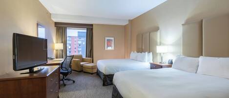 Habitación de hotel con dos camas, un escritorio con televisor, una silla, una lámpara y una ventana con cortinas.
