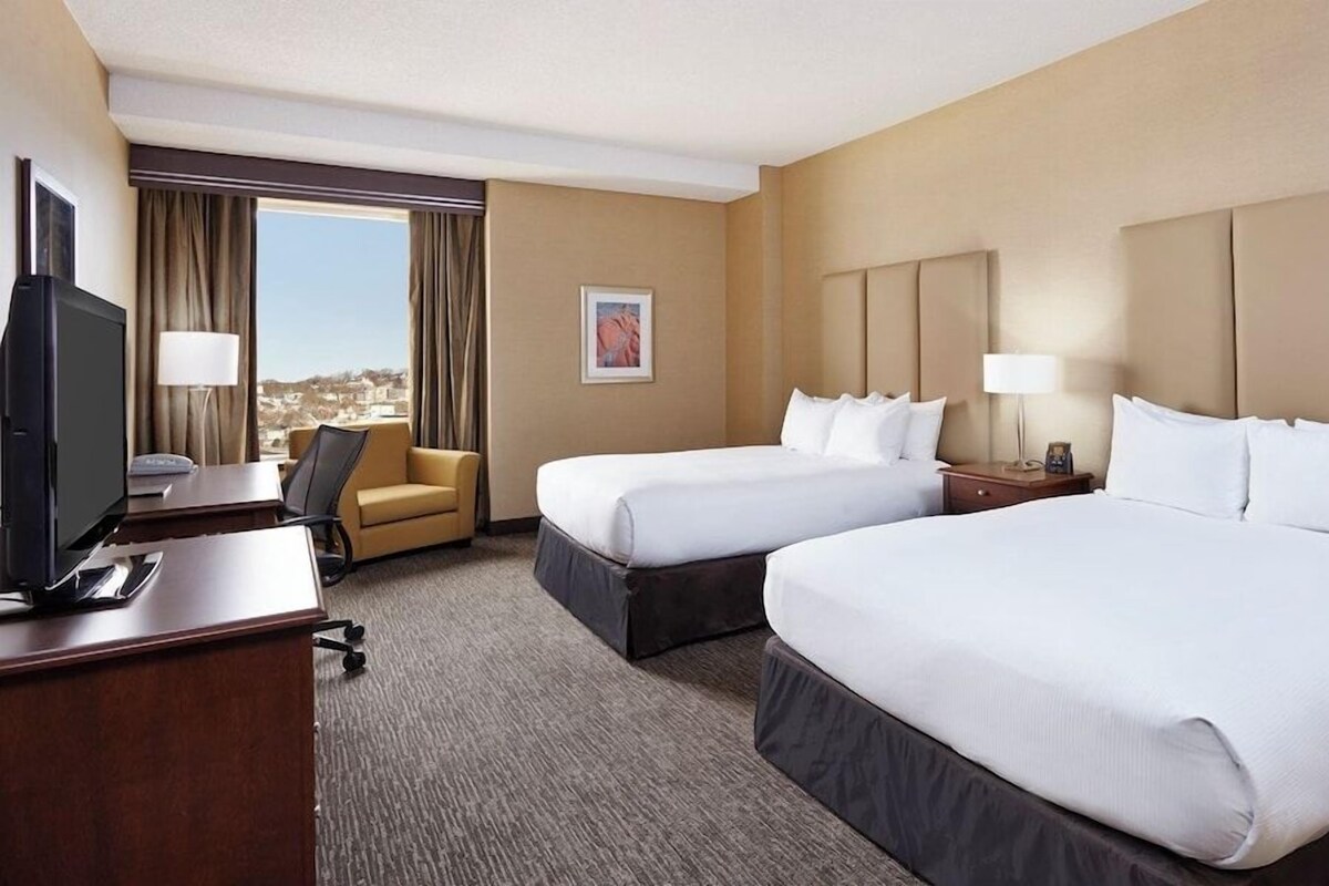 A hotel room with two beds, a desk, a chair, and a television.