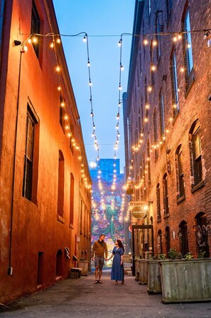A narrow alleyway with brick buildings, string lights, and a mural in the distance. - Saint John Harbourfront Hotel (Saint John)
