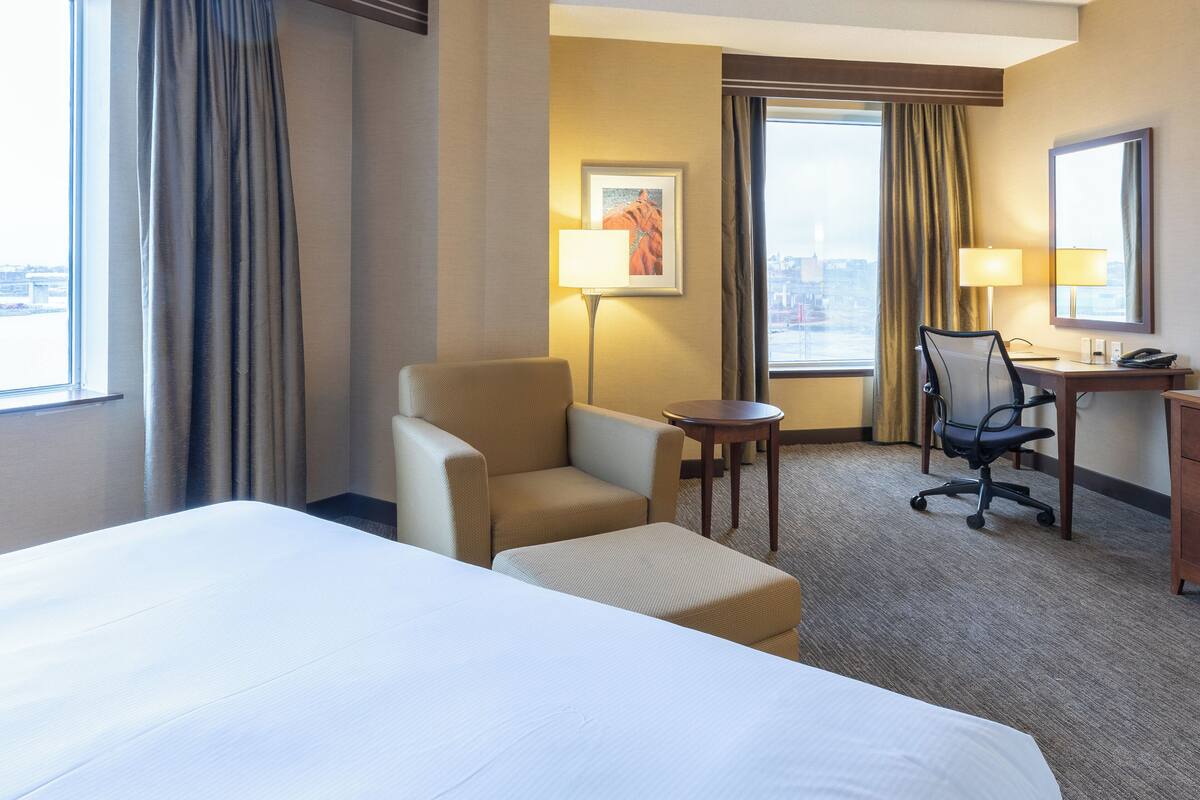 A hotel room with a bed, two armchairs, a desk with a chair, a lamp, and a framed picture on the wall.