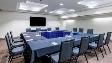 A conference room with a long table, chairs, a flat-screen TV, and ceiling lights.