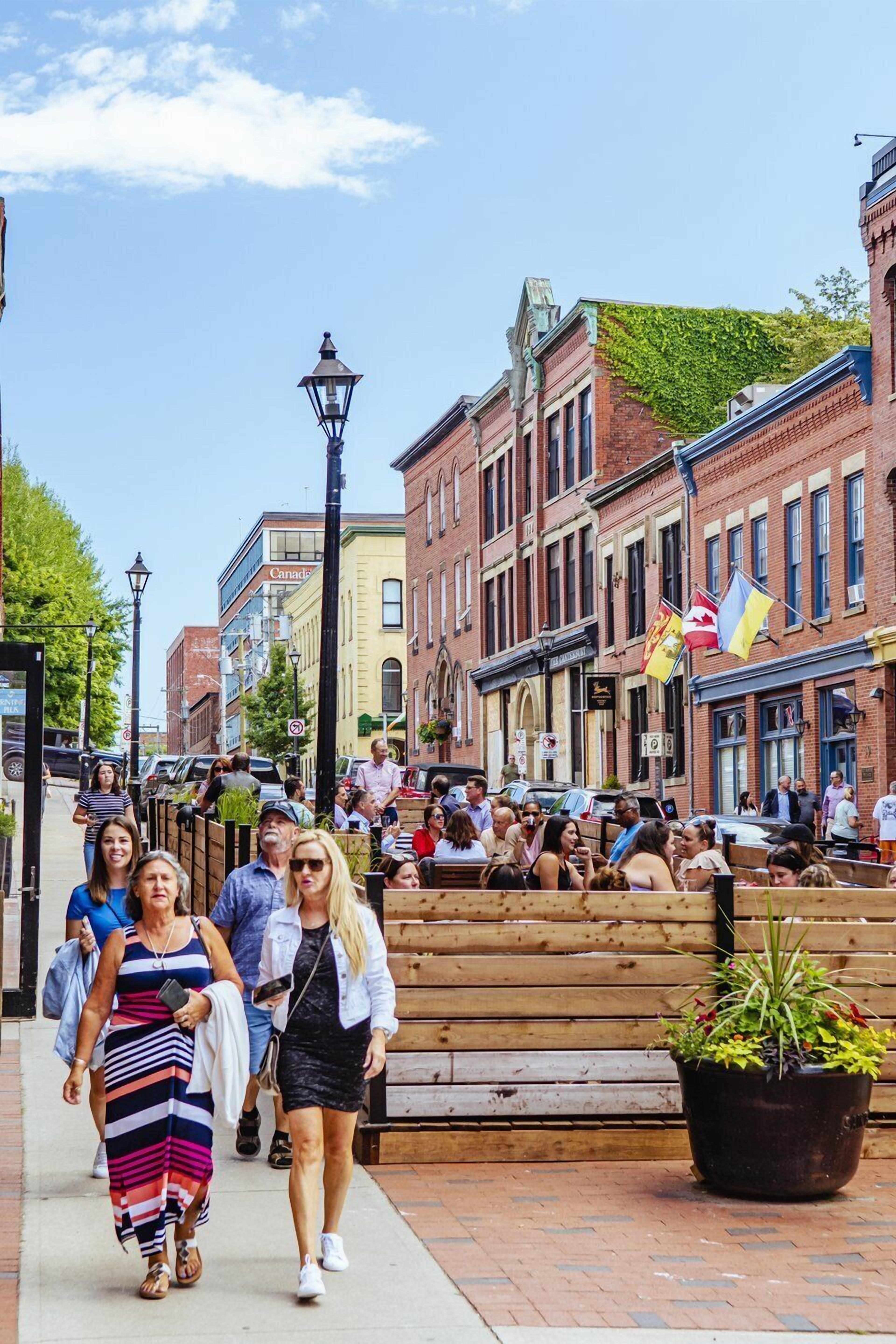 A busy street with pedestrians, historic buildings, and a wooden bench with a planter.