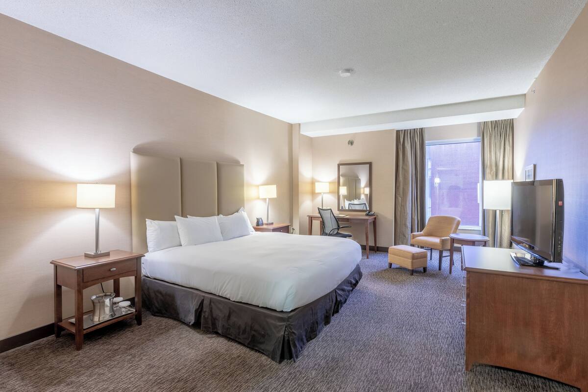 A hotel room with a large bed, bedside lamps, a desk with a chair, a television, and a window with curtains.