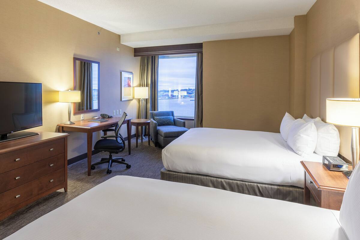 A hotel room with two beds, a desk with a chair, a television, and a window with a view.