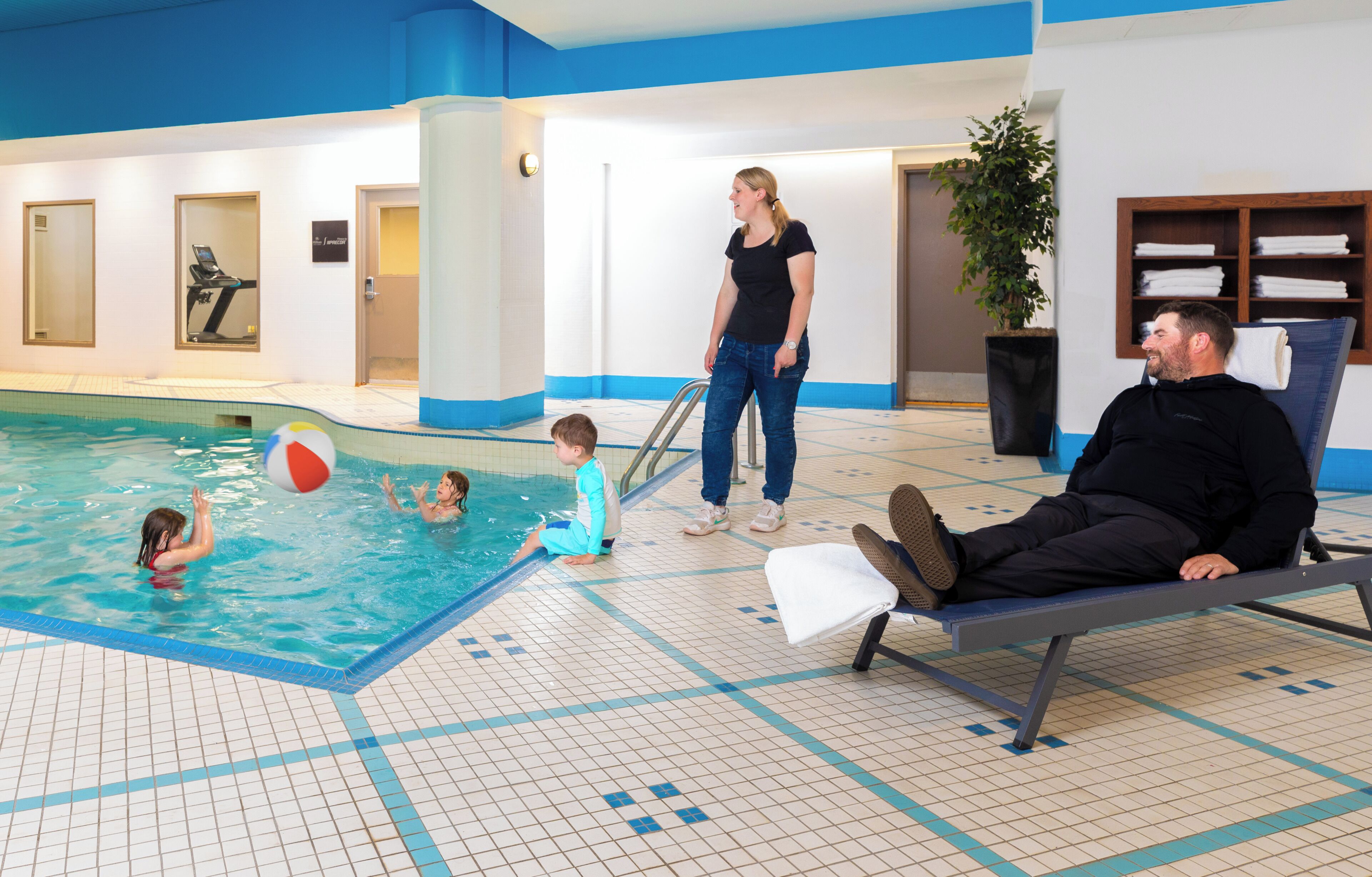 Una piscina interior con suelo de baldosas, un banco y una persona sentada allí.