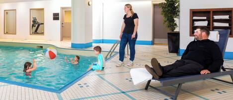 Una piscina interior con suelo de baldosas, un banco y una persona sentada allí.