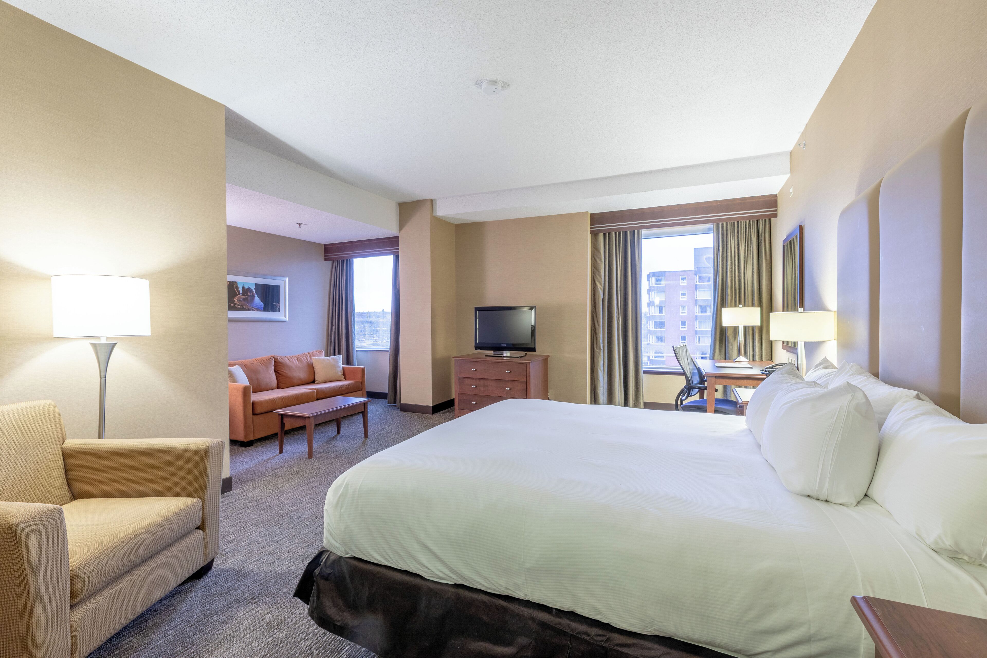 A hotel room with a large bed, a desk, a chair, a sofa, a television, and a window with curtains.