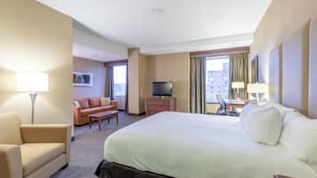 A hotel room with a large bed, a desk, a chair, a sofa, a television, and a window with curtains.