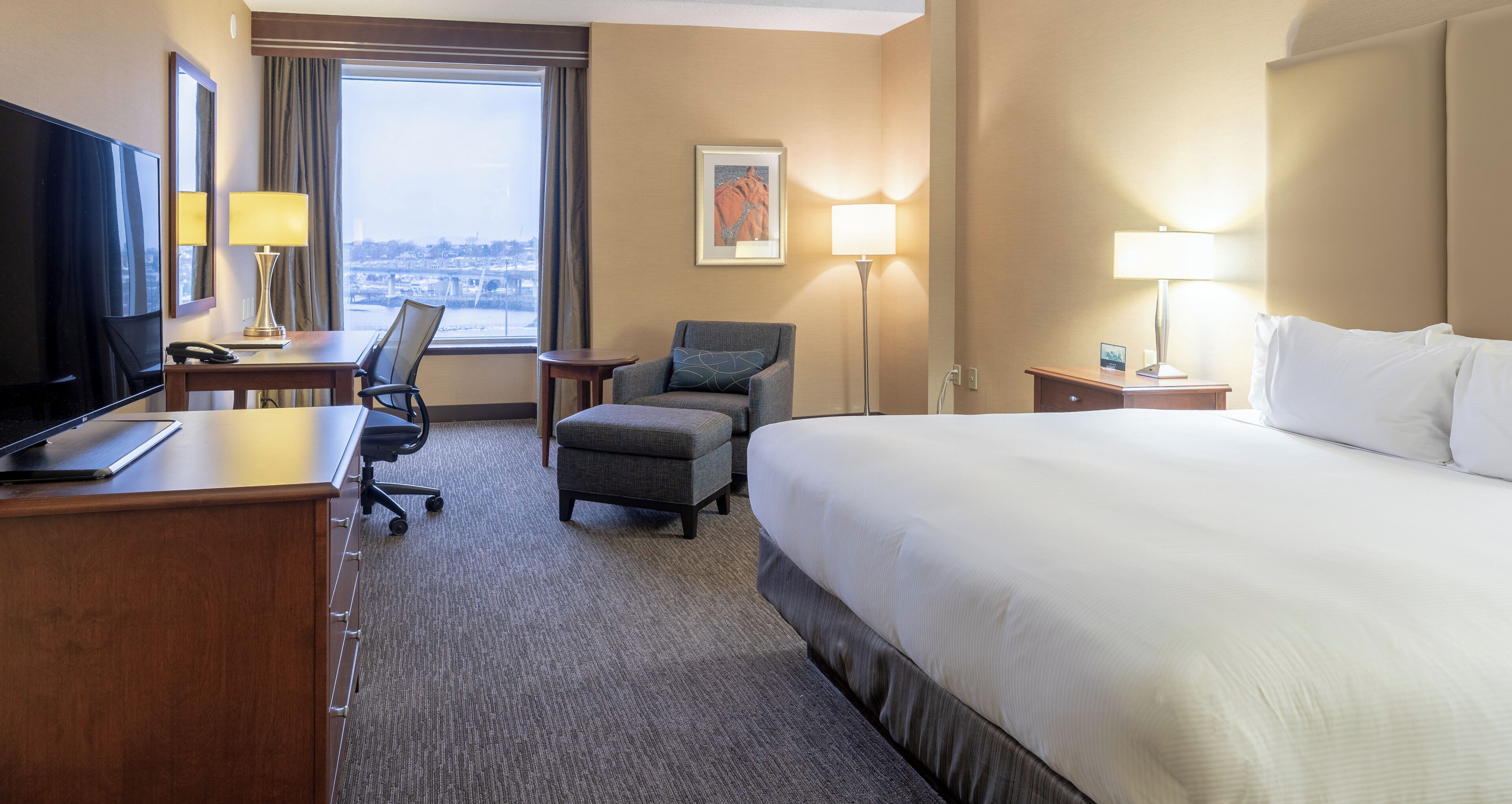 A hotel room with a bed, desk, chair, and a television.