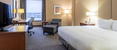A hotel room with a bed, desk, chair, TV, and a window with a city view.