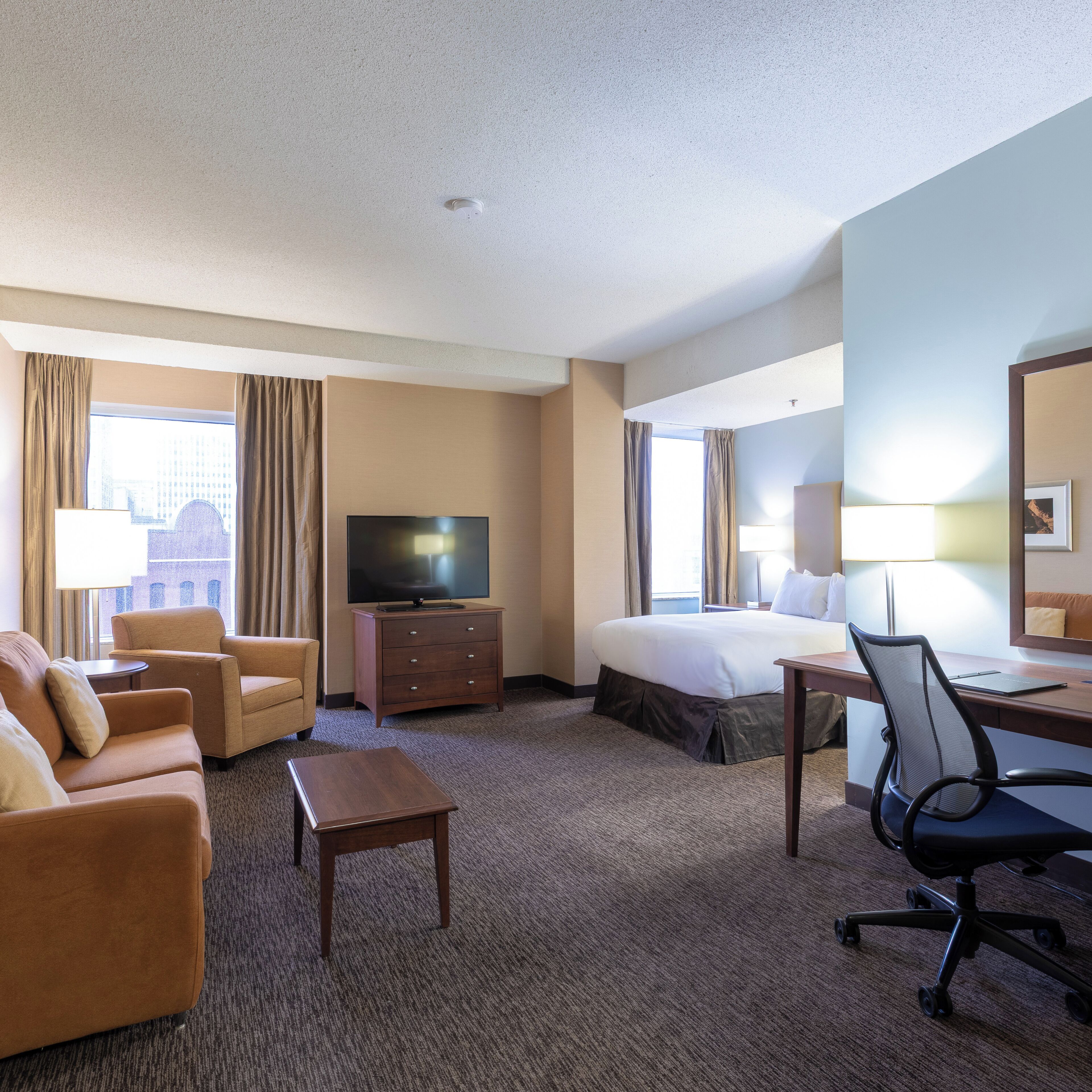 A hotel room with a bed, a desk, a chair, a television, and a sofa.