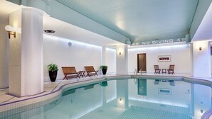 A modern indoor swimming pool with clear water, surrounded by lounge chairs and potted plants.