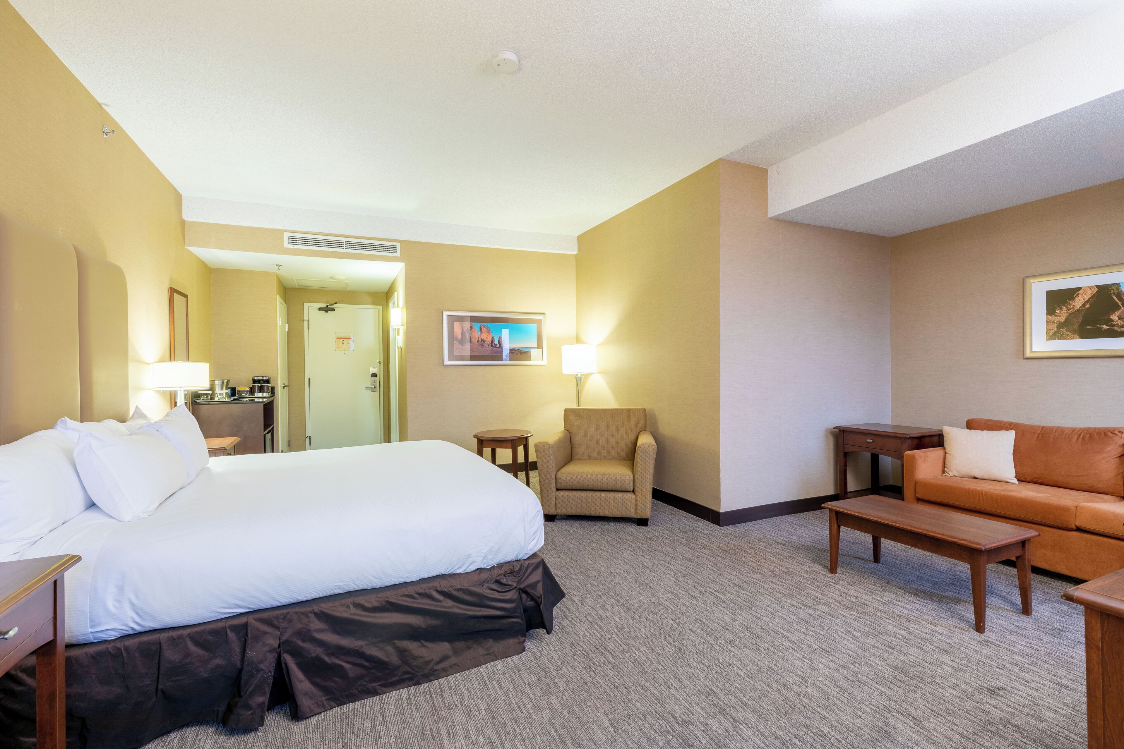 A hotel room with a bed, a sofa, a small table, a chair, and a lamp.