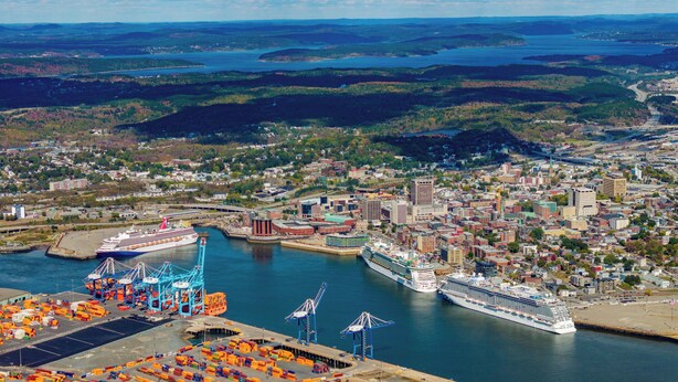 A coastal city with a large cruise ship docked, a busy port with cargo containers, and a bridge connecting two land masses.