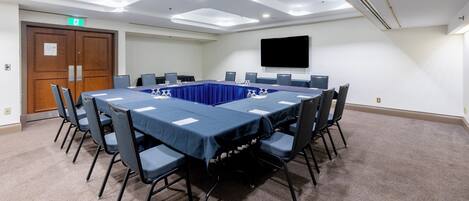 Un salón de conferencias con una larga mesa, sillas, un televisor de pantalla plana y una puerta con letrero de salida.