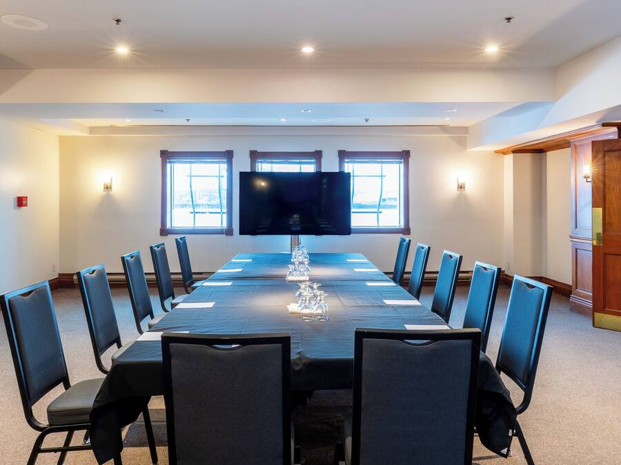 Uma sala de conferências com uma mesa comprida, cadeiras, uma TV de tela plana, janelas e portas de madeira.