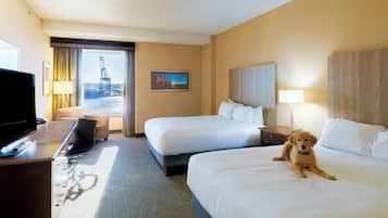 A hotel room with two beds, a TV, a desk, and a view of a bridge.