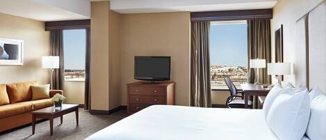 A hotel room with a large bed, a television on a wooden cabinet, a desk with a chair, and a sofa.