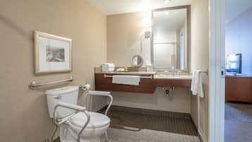 A bathroom with a toilet, handrail, sink, mirror, towel rack, and a framed picture on the wall.