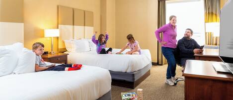 A hotel room with two beds, a desk, and a window.
