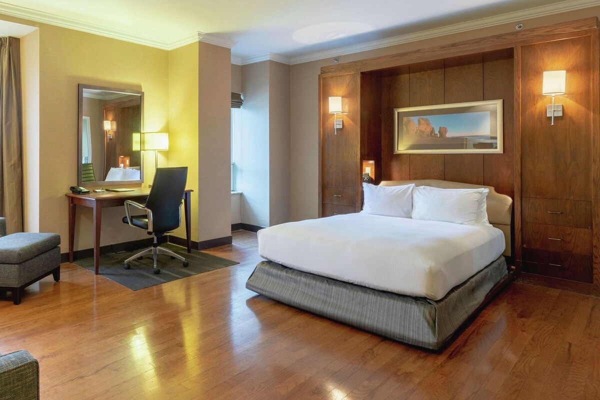 A hotel room with a large bed, a desk, a chair, and a sofa.