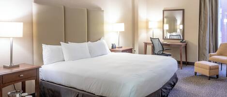 Habitación de hotel con una cama grande, lámparas de noche, un escritorio con silla, una mesita y un espejo.