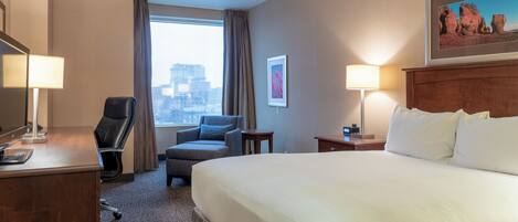 Habitación de hotel con cama, escritorio, silla, lámpara y vistas a la ciudad por la ventana.