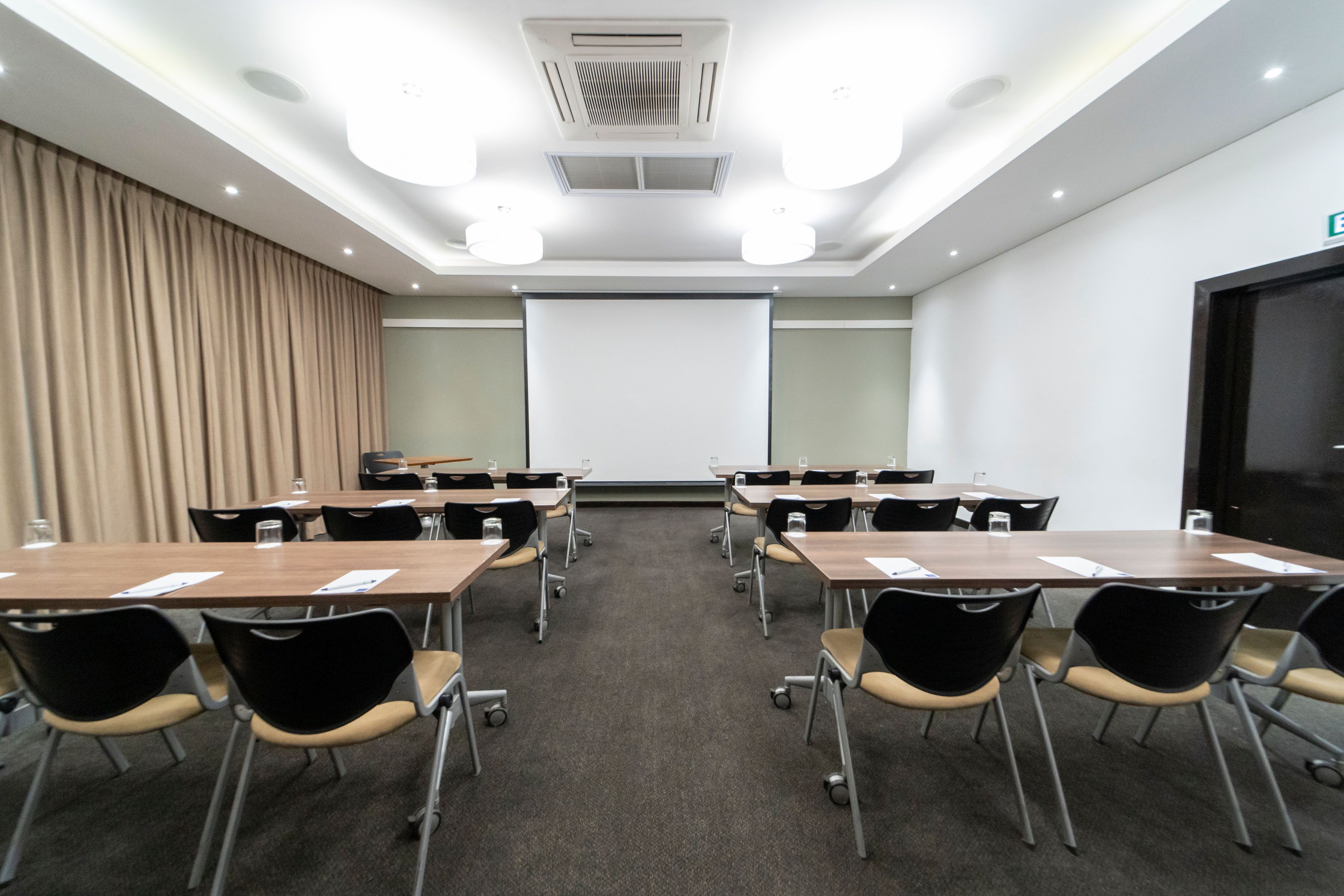 Un salón de conferencias con pantalla de proyector, mesas y sillas.