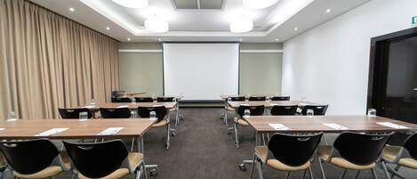Un salón de conferencias con pantalla de proyector, mesas y sillas.