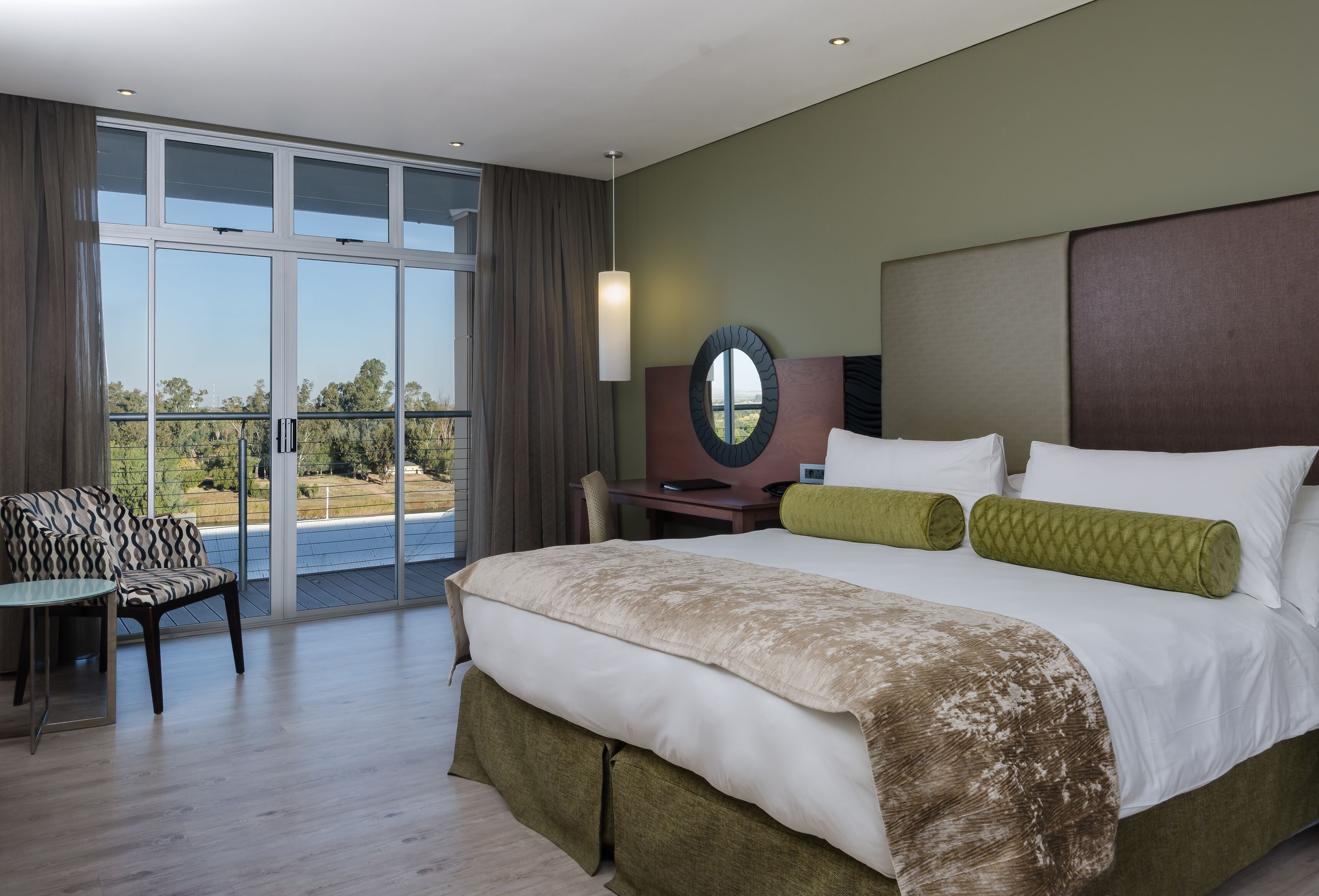 Een hotelkamer met een groot bed, een bureau, een stoel en uitzicht op de omgeving door een schuifdeur.