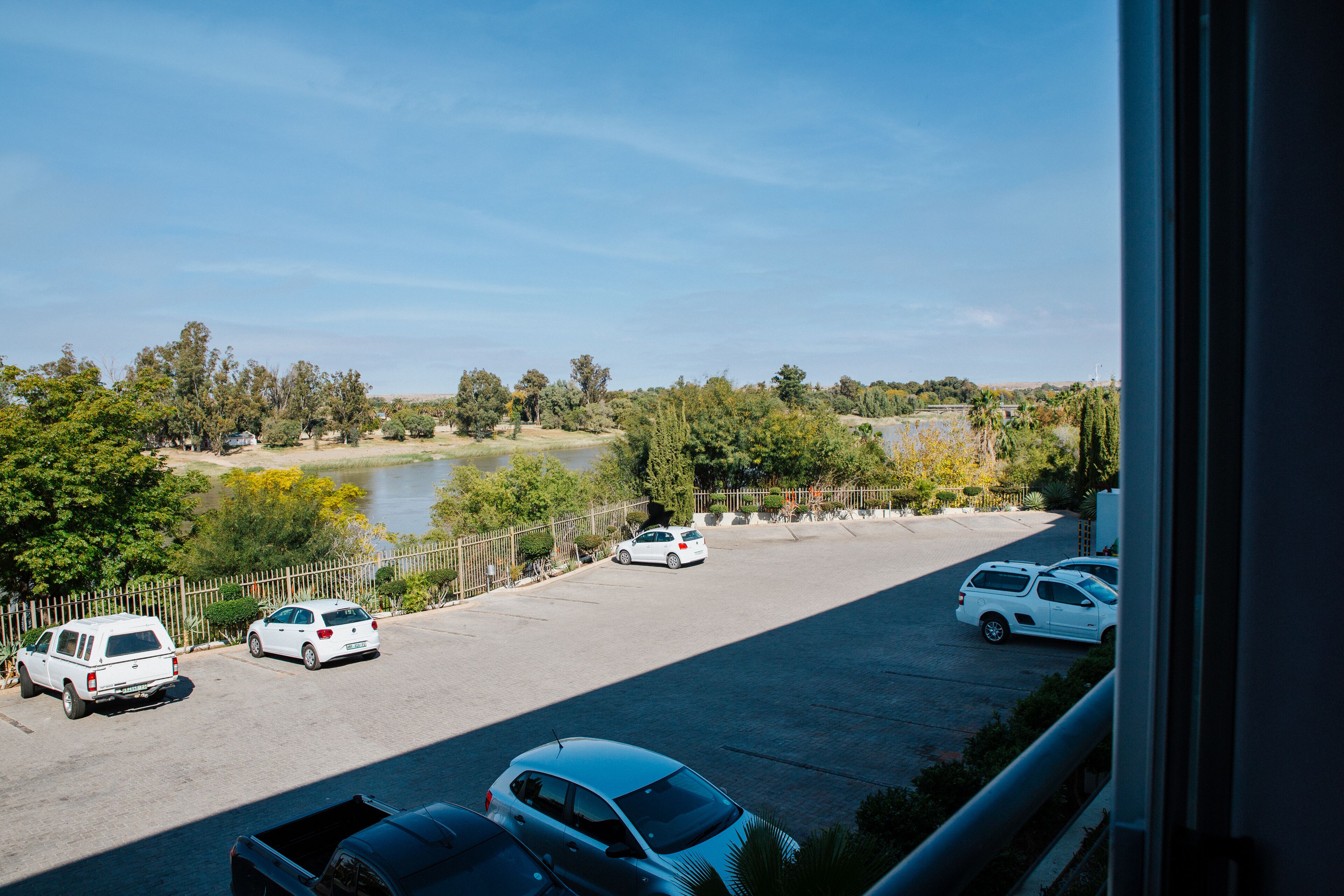 A parking lot with several cars, a body of water, and trees in the background.
