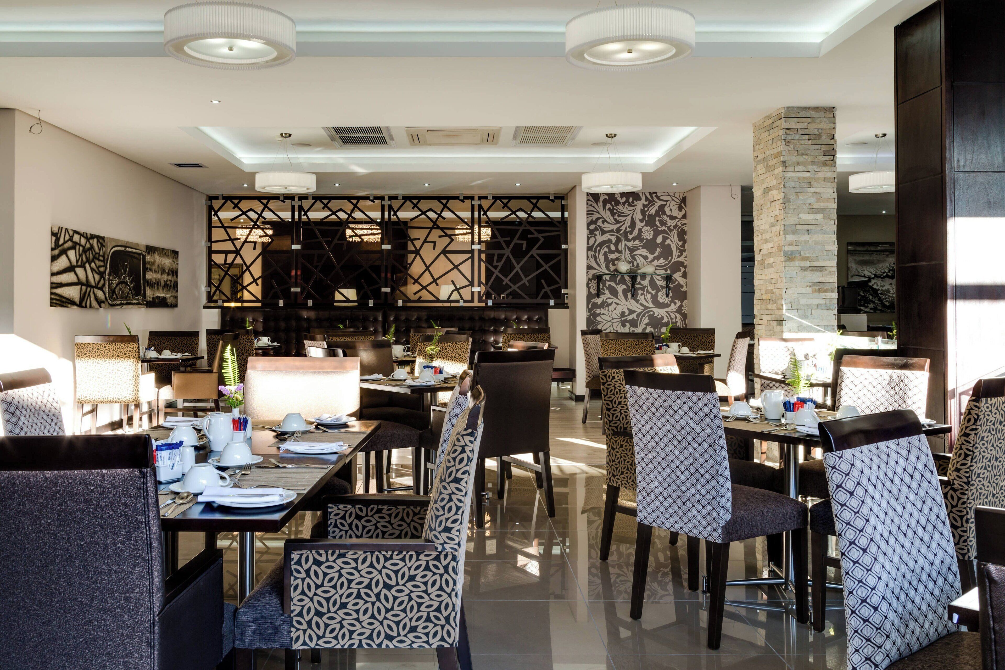 A modern dining area with tables and chairs, a decorative wall, and a kitchen in the background.
