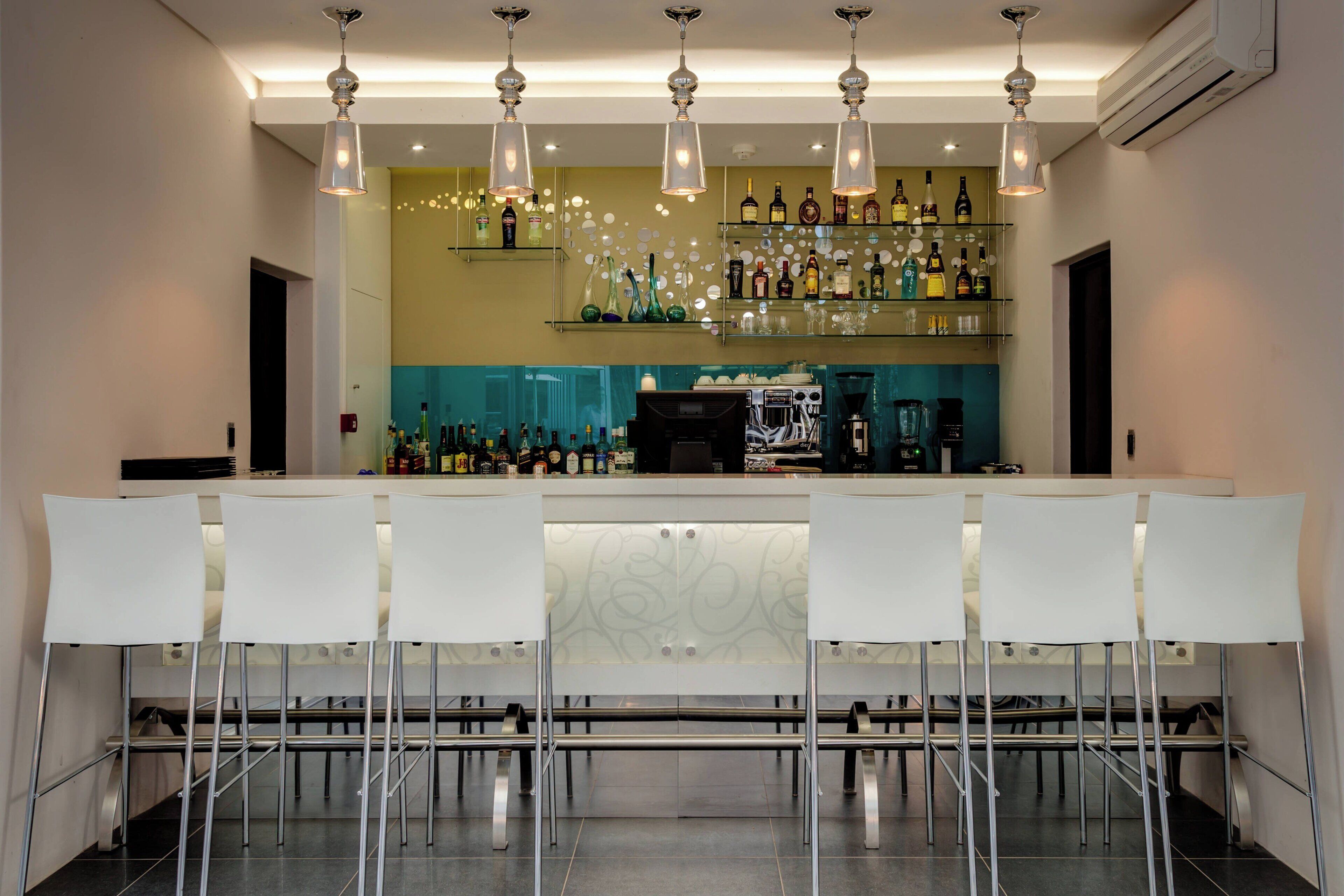A bar area with white bar stools, a counter, and shelves stocked with bottles.