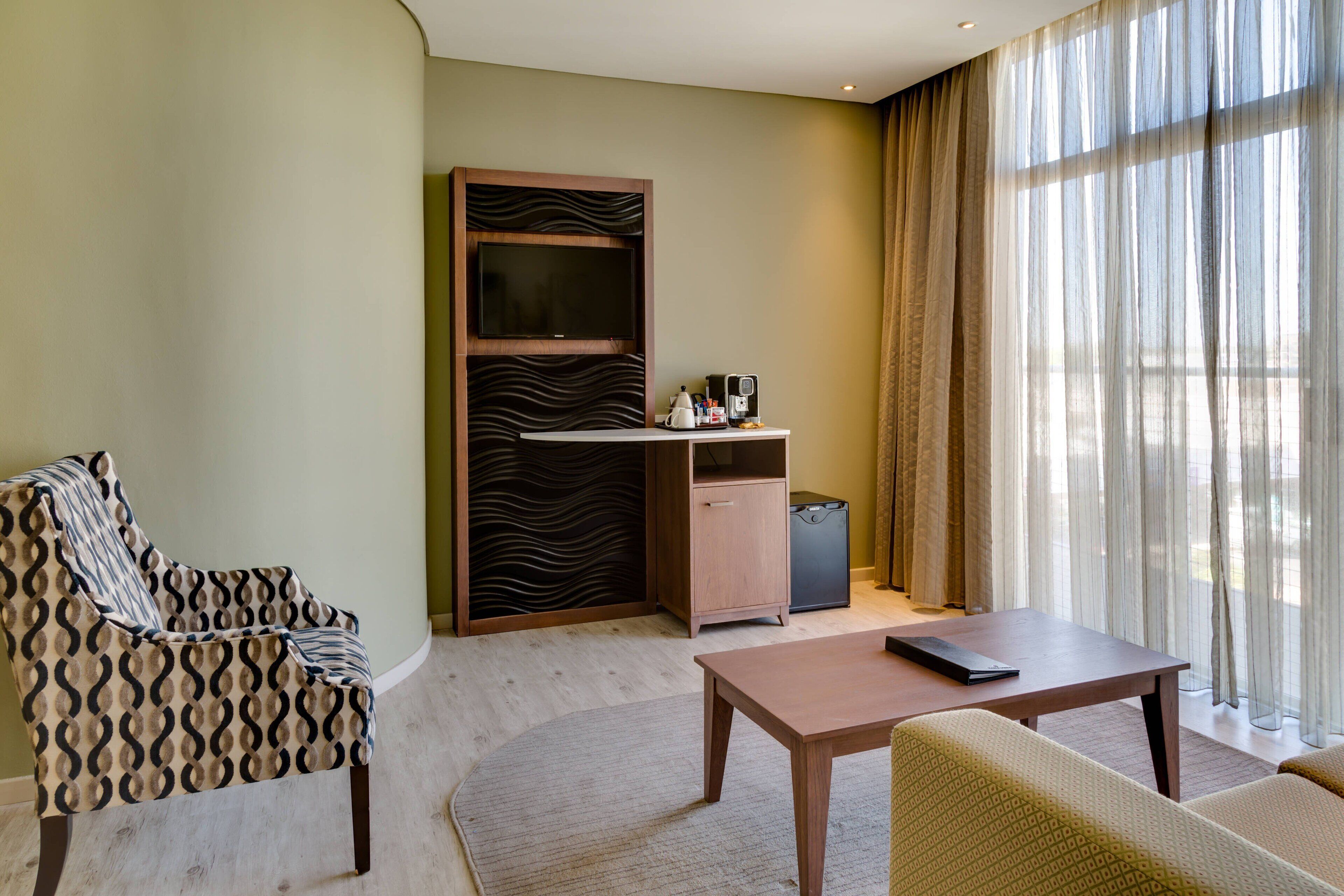 A hotel room with a sofa, a small table, a cabinet, and a TV.
