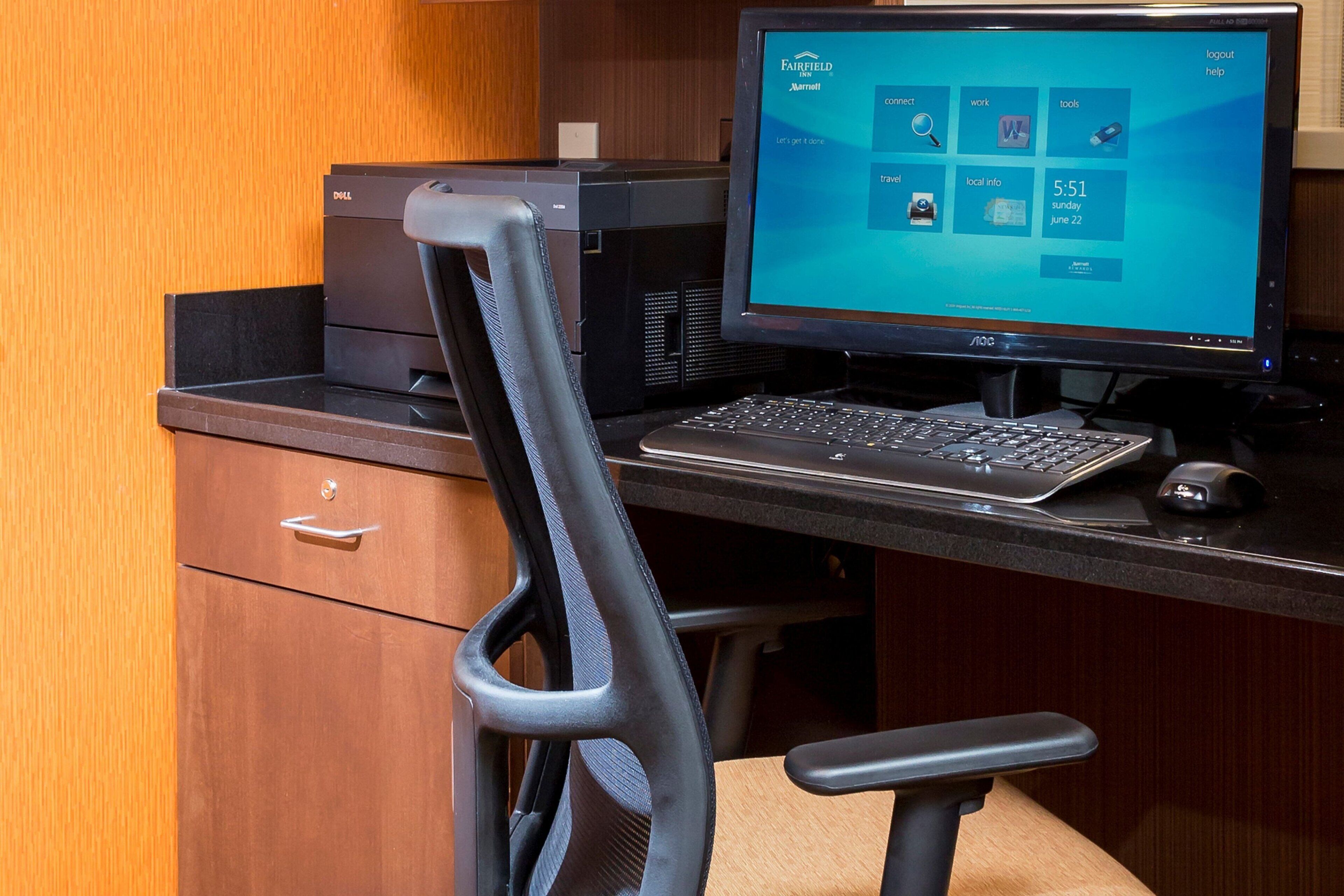 Un escritorio con un monitor Dell, teclado y ratón, una silla de oficina negra y un armario de madera.