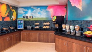 Une cuisine avec un plan de travail noir, des armoires en bois, un présentoir pour les aliments et une fresque murale.