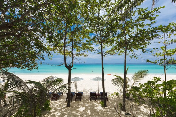 Een privéstrand, wit zand, ligstoelen aan het strand, parasols