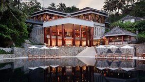 A luxurious resort with a reflective pool, a two-story building with a bar area, and outdoor seating.