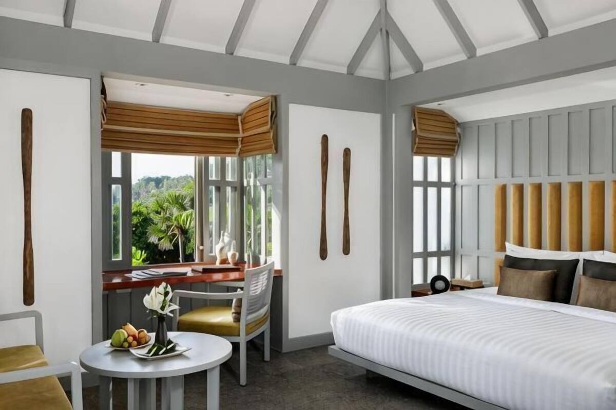 A hotel room with a bed, a desk with a chair, a round table with a chair, and large windows.