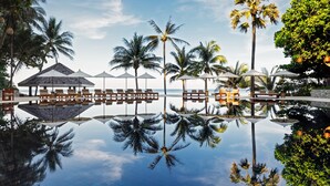 A serene pool area with lounge chairs and umbrellas, surrounded by palm trees and a clear view of the ocean. - The Surin Phuket (Choeng Thale)