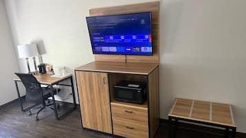 A hotel room with a wooden desk, a television mounted on a wooden cabinet, a small table, and a chair.