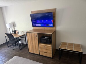 Habitación de hotel con un escritorio de madera, un televisor instalado en un mueble de madera, una mesita y una silla.