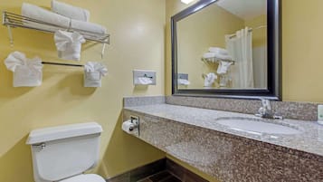 A bathroom with a toilet, sink, mirror, towel rack, and a towel dispenser.