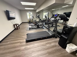 Academia com equipamentos de cardio, espelho e bebedouro.