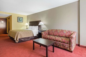 Una habitación de hotel con cama, sofá, mesa y dos lámparas.