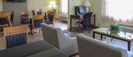 A hotel room with a TV, a desk with a computer, a sofa, and several chairs.