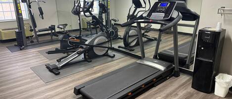 Un gimnasio con máquinas de cardio, equipo de pesas y un dispensador de agua.