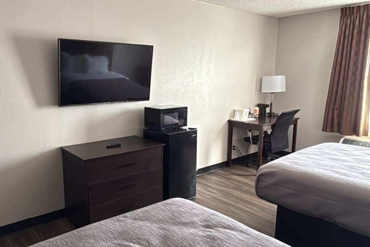 Habitación de hotel con cama, escritorio con silla, televisor montado en la pared y microondas en el escritorio.