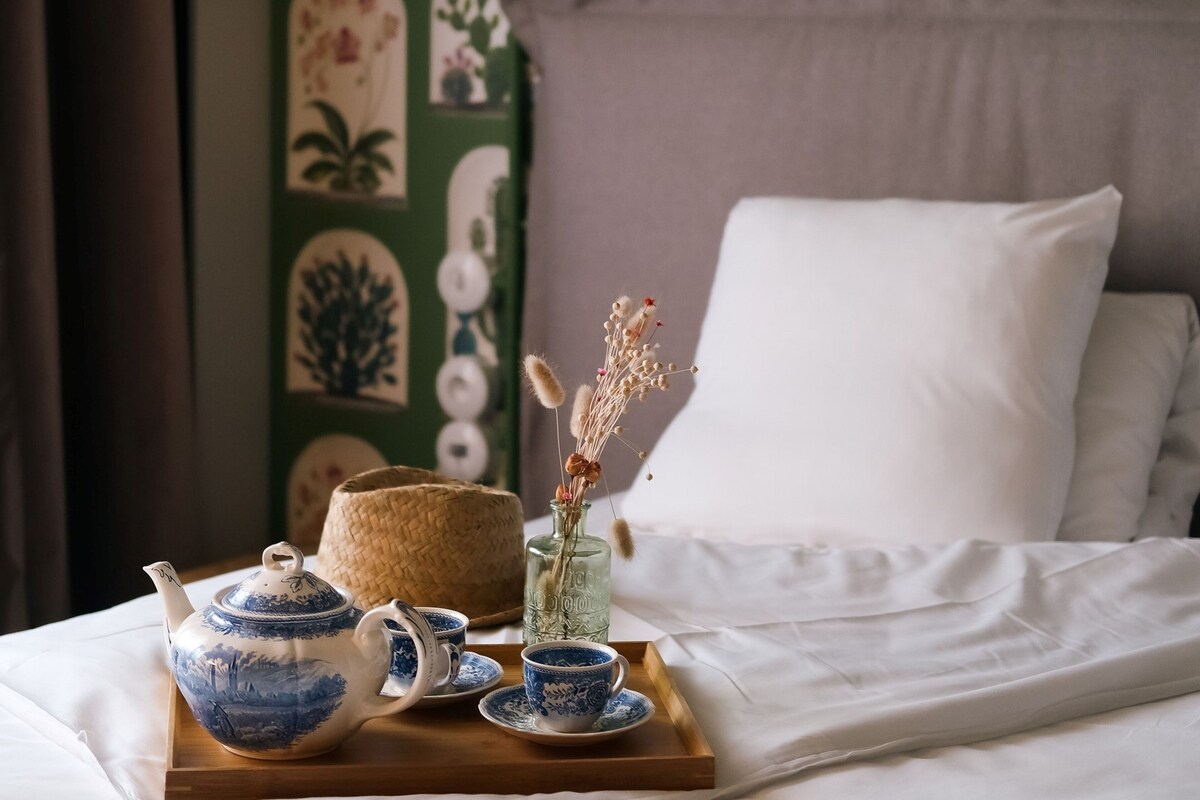 A neatly arranged tea set on a wooden tray on a bed with white linens.