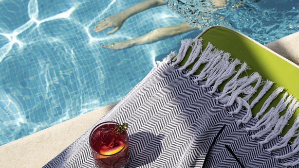 Blick auf einen Pool mit einem Getränk, einem Handtuch und Füßen im Wasser.